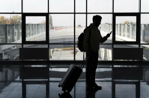 "Traveler at airport with suitcase, waiting for Melbourne airport transfer and chauffeur services, luxury car hire options."